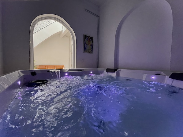 Een bubbelbad met waterstralen, een houten bank en een schilderij aan de muur.