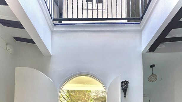 Decoração moderna com um arco central que dá para uma área de piscina, tudo ladeado por paredes brancas e uma escadaria.