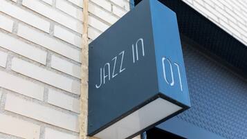 Segno nero con scritta bianca che riporta "JAZZ IN 01" fissato a un muro in mattoni.
