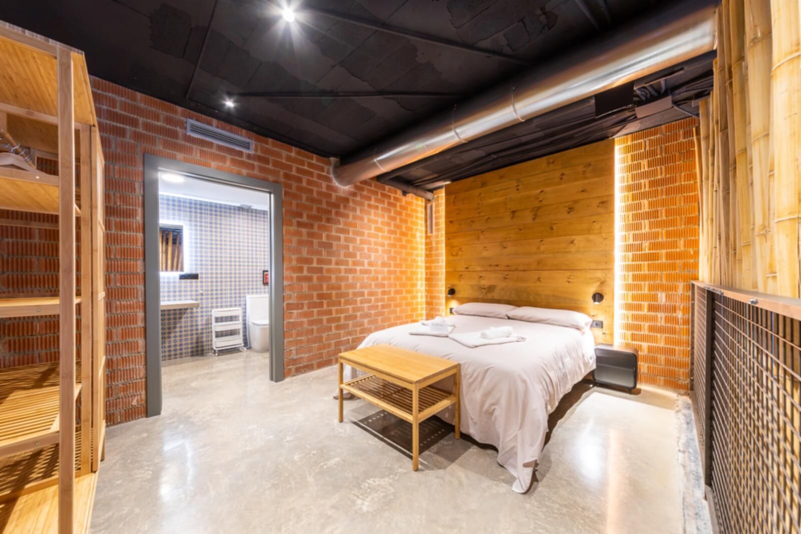 Un dormitorio moderno con pared de ladrillo, cabecero de madera y un banco.