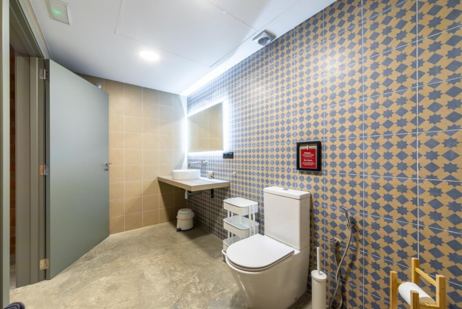 Un baño con inodoro, lavamanos y espejo. Las paredes tienen un diseño geométrico de azulejos.