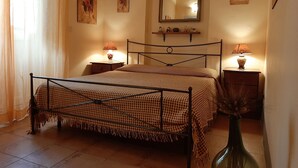 A bedroom with a metal bed frame, two bedside tables with lamps, a mirror above the bed, and artwork on the walls. - Tangerine house by the sea (Riposto)