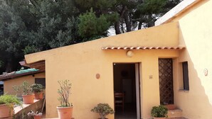 A yellow building with a tiled entrance, potted plants, and a stone pathway. - Tangerine house by the sea (Riposto)