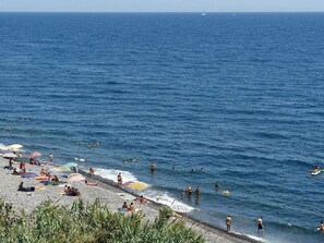 A beach with people swimming and sunbathing, umbrellas, and a clear blue sky.