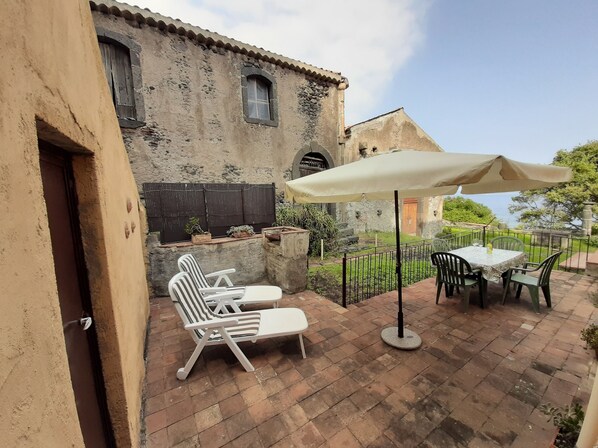 A patio with a table and chairs, a large umbrella, and a rustic building in the background.