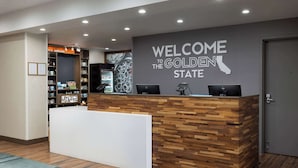 A reception desk with a "Welcome to the Golden State" sign, a wooden reception area, and a coffee station with various mugs and cups. - Hampton Inn Oakhurst-yosemite, CA (Oakhurst)