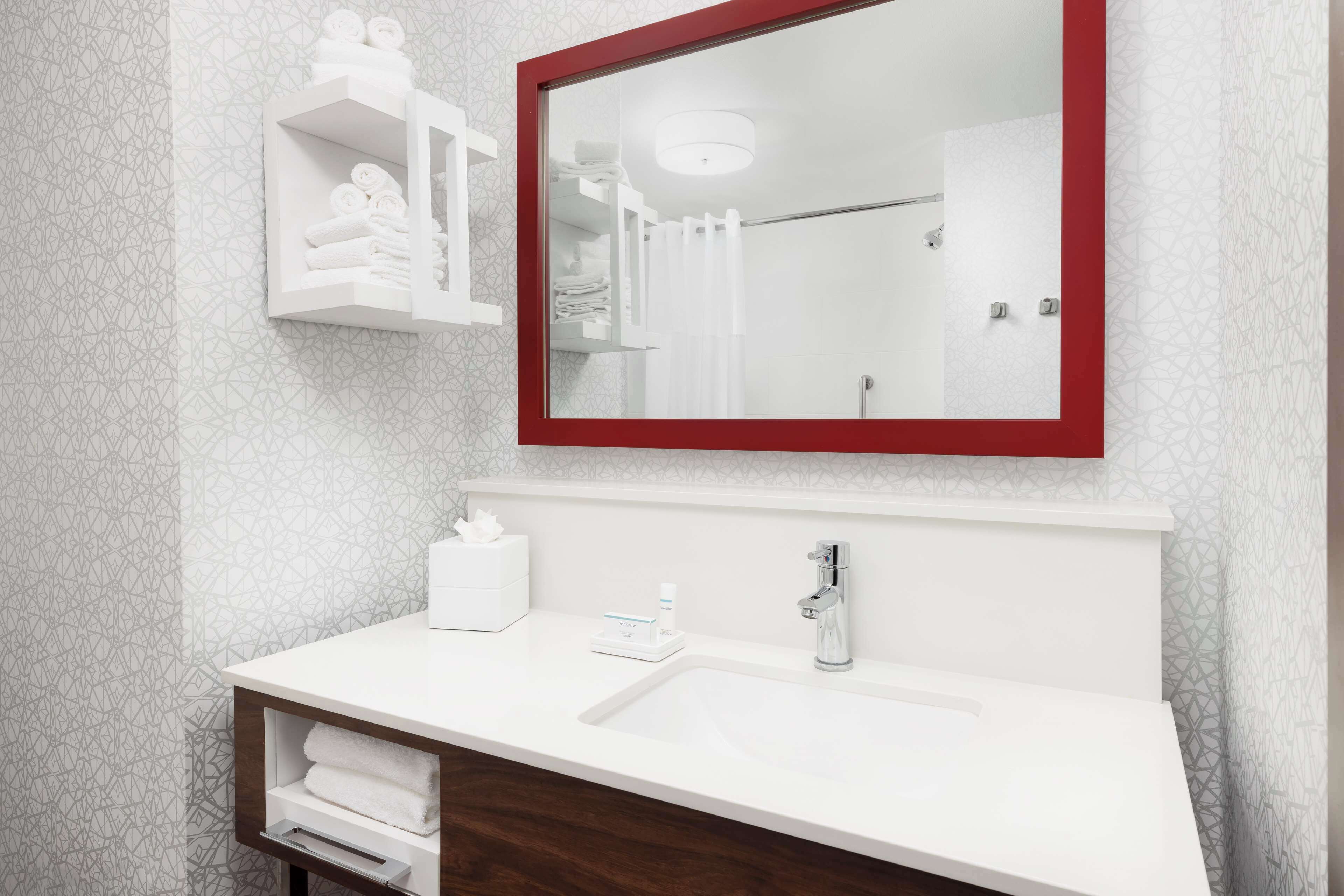 A bathroom with a white sink, a mirror with a red frame, and a towel rack with folded towels.
