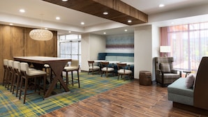 A modern hotel lobby with a wooden reception desk, bar stools, a sofa, and a patterned carpet. - Hampton Inn Oakhurst-yosemite, CA (Oakhurst)