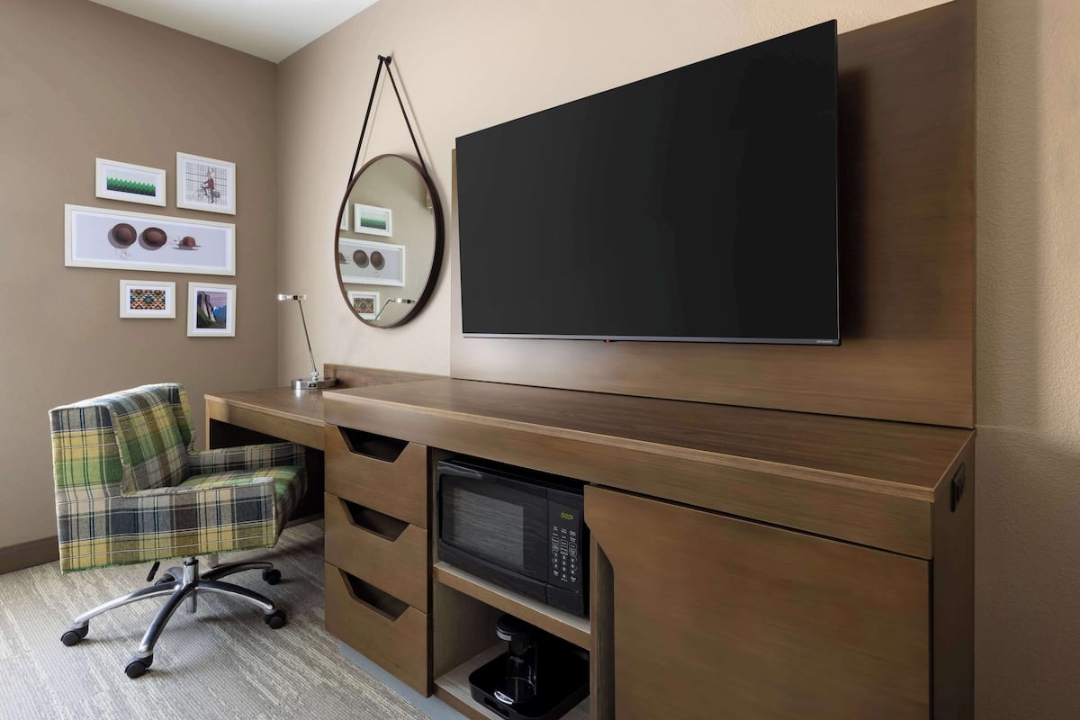 Un espace de bureau moderne doté d’un grand téléviseur à écran plat, d’un fauteuil de bureau à carreaux, d’un bureau avec un micro-ondes intégré et d’œuvres d’art accrochées au mur.