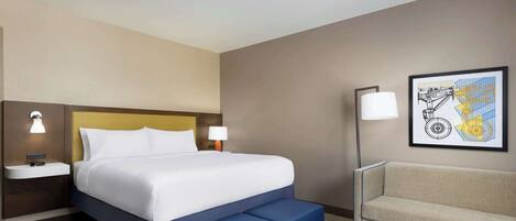 Una habitación de hotel con cama, mesitas de noche, sofá y lámpara de pared.