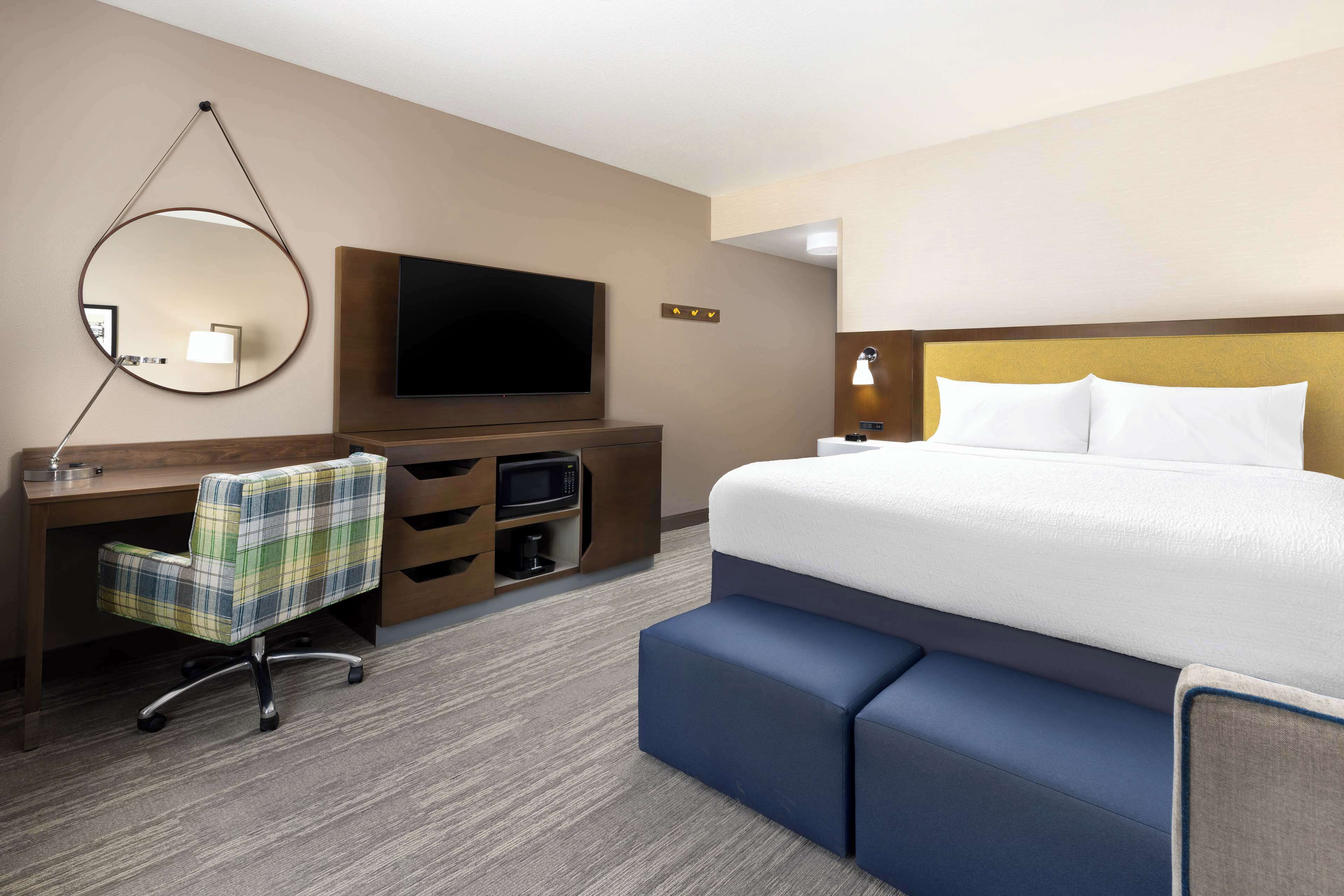 Een hotelkamer met een groot bed, een bureau met stoel, een flatscreen televisie, een magnetron en een klein tafeltje met lamp.