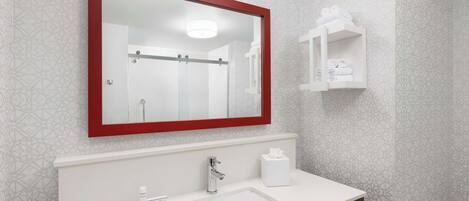 Un baño moderno con un espejo grande, un lavamanos, un perchero para toallas y un estante pequeño con artículos de aseo.