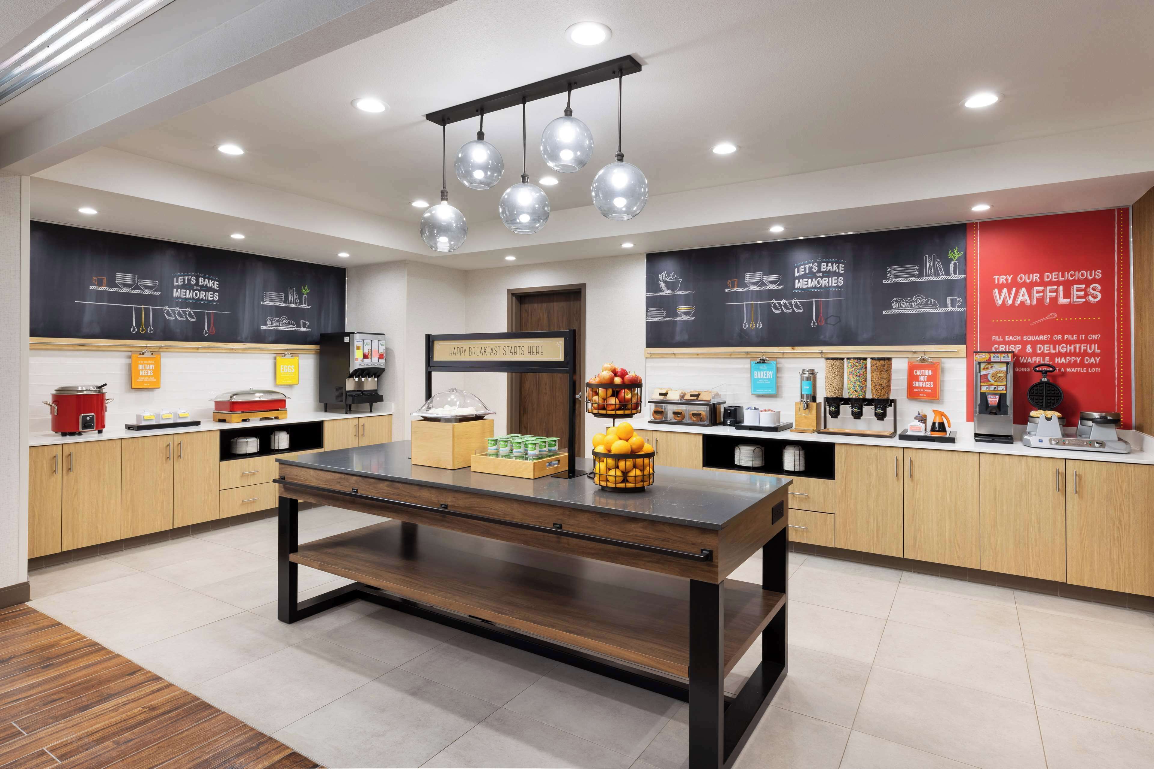 A modern kitchen with wooden cabinets, a central island, and a chalkboard wall with menu items.