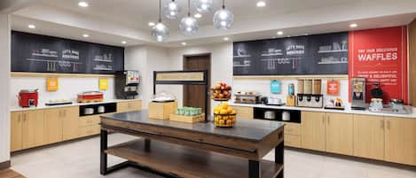 Una cocina moderna con armarios de madera, una isla central y una pared de pizarra con opciones de menú.