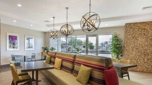 Un espace repas moderne avec un long banc, une table et des chaises. On y trouve des luminaires suspendus et une vue sur l’extérieur.
