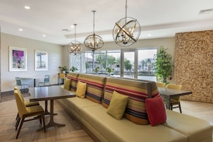 Un comedor moderno con un largo banco, una mesa y sillas. Hay luces colgantes y vistas al exterior.