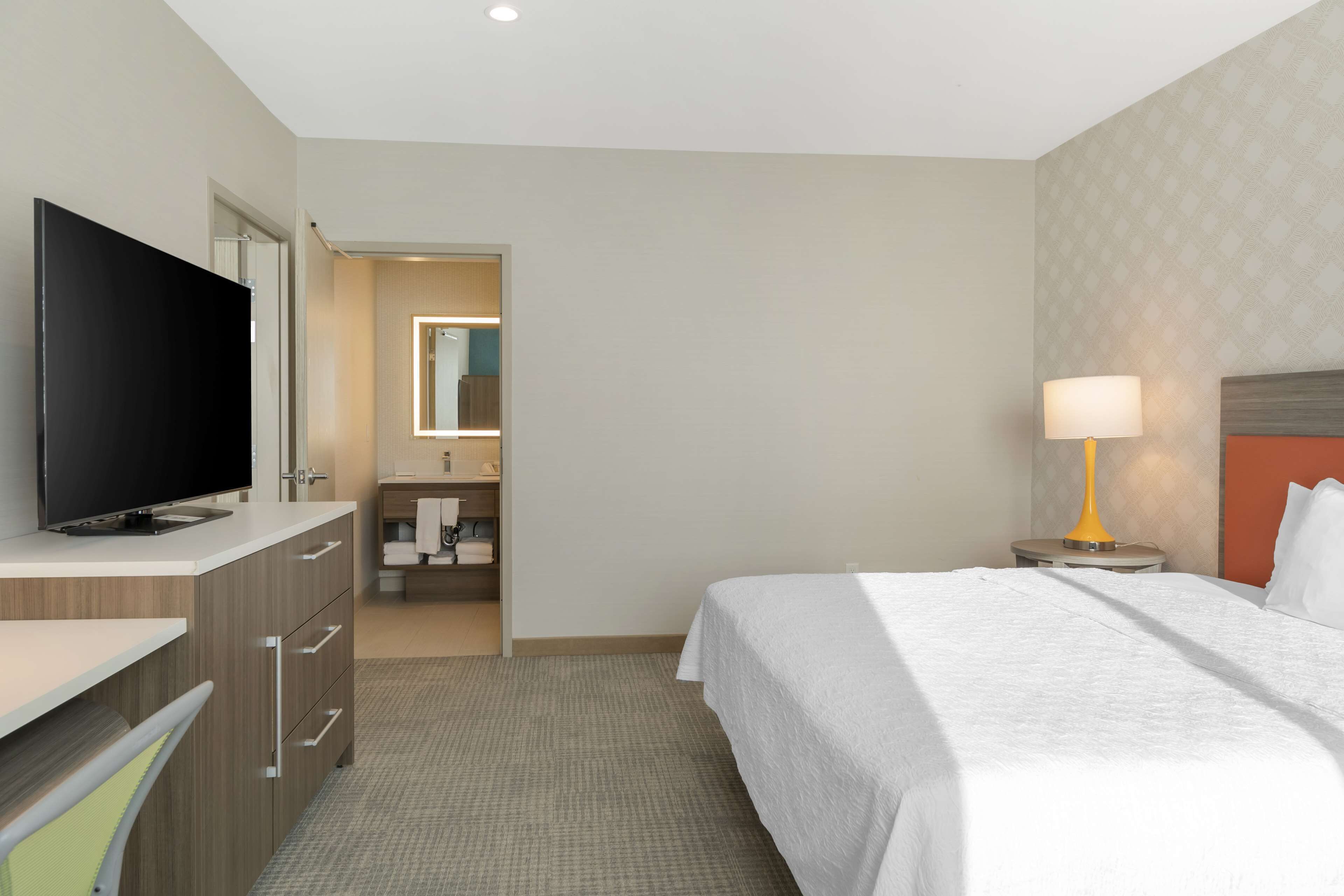A hotel room with a bed, a TV, a desk, a lamp, and a bathroom visible through an open door.