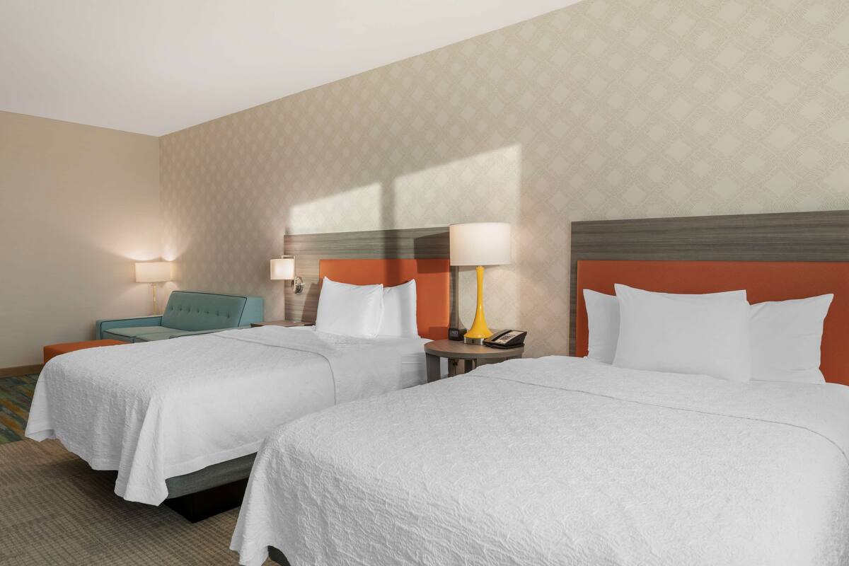 Una habitación de hotel con dos camas, una mesita, una silla y una lámpara.