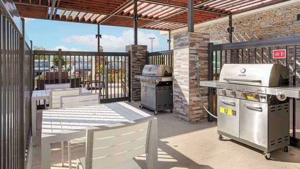 Une terrasse extérieure dotée d’un espace salon couvert, d’un coin barbecue et d’un mur en pierre servant de décor.