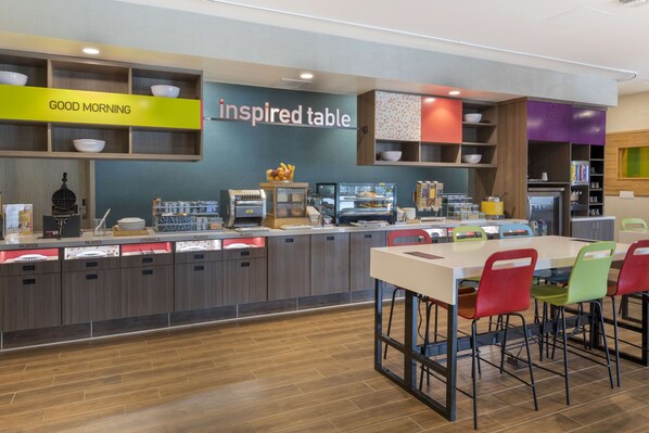 Un área de cocina moderna con un mostrador que exhibe platos, utensilios y tazones. Hay un letrero que dice “GOOD MORNING” y otro que dice “inspired table”.