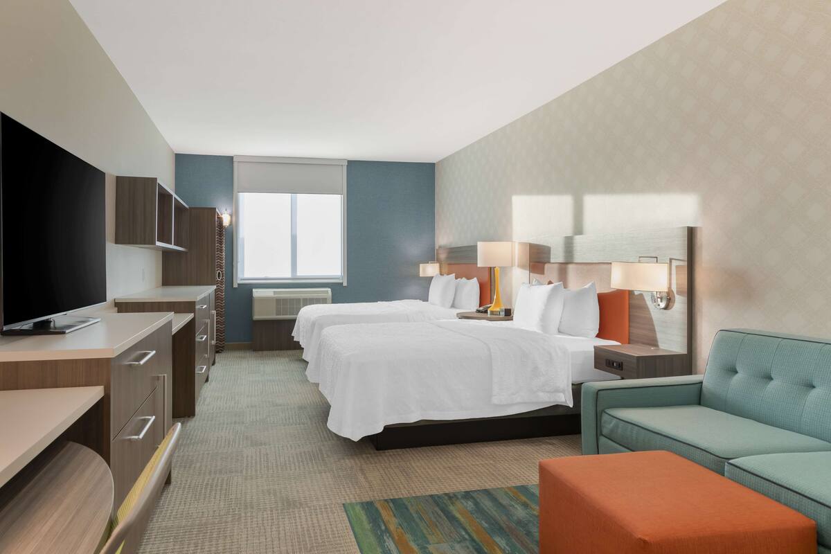 Una habitación de hotel con cama, dos mesitas de noche, televisión, sofá y ventana.