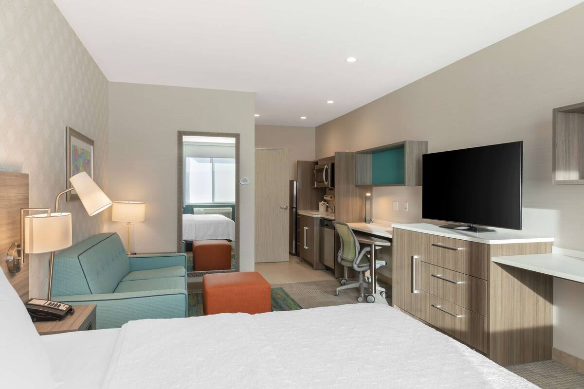 Habitación de hotel con cama, escritorio, televisor, kitchenette y baño.