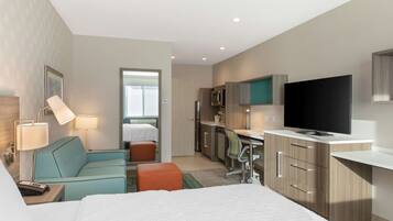 A hotel room with a bed, a desk, a TV, a kitchenette, and a bathroom.