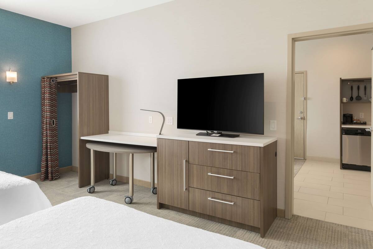 Una habitación de hotel con cama, escritorio con televisor, armario y kitchenette.