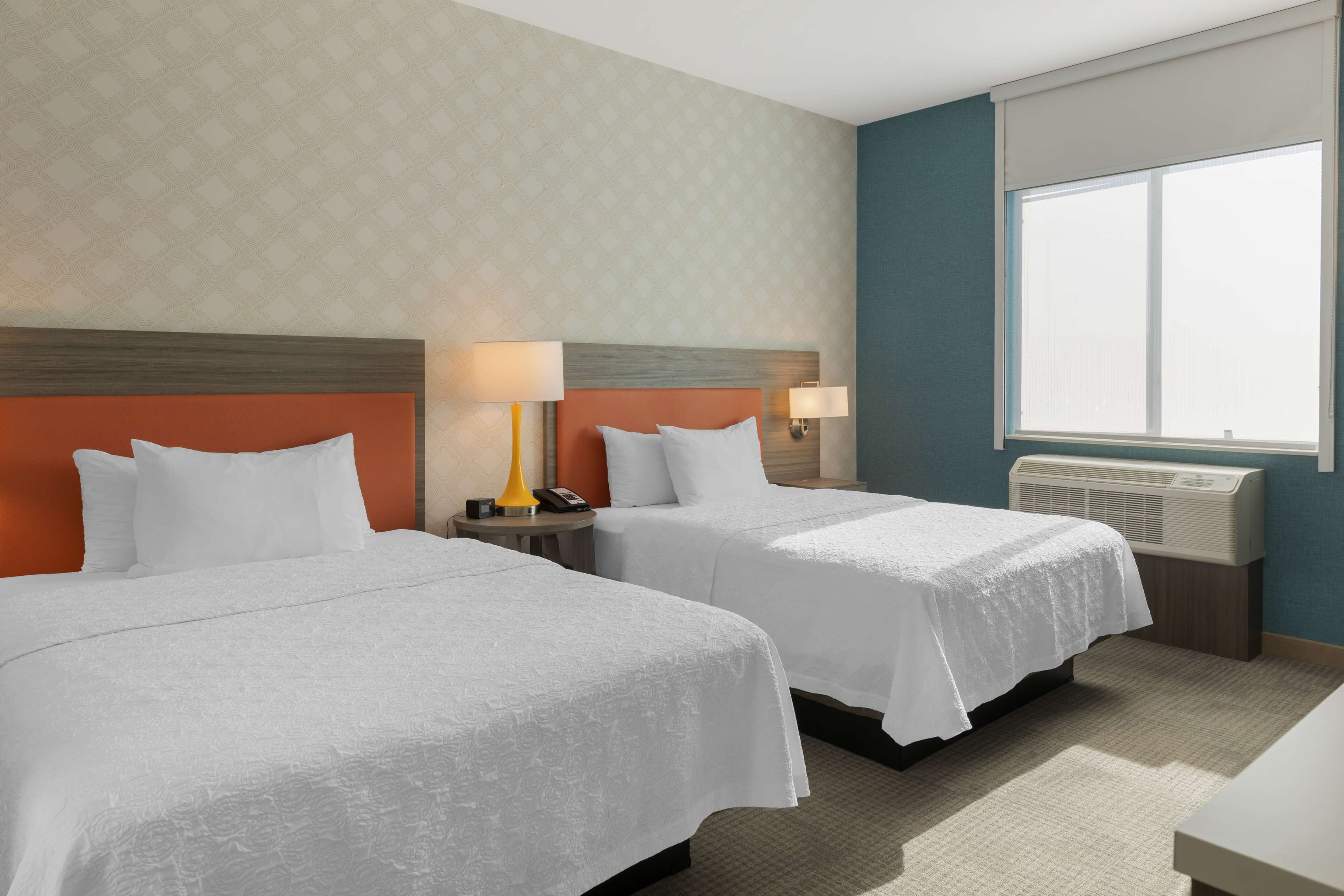 Ein Hotelzimmer mit zwei Betten, einem großen Fenster, einer Wandheizung und einem gemusterten Wandpapier.