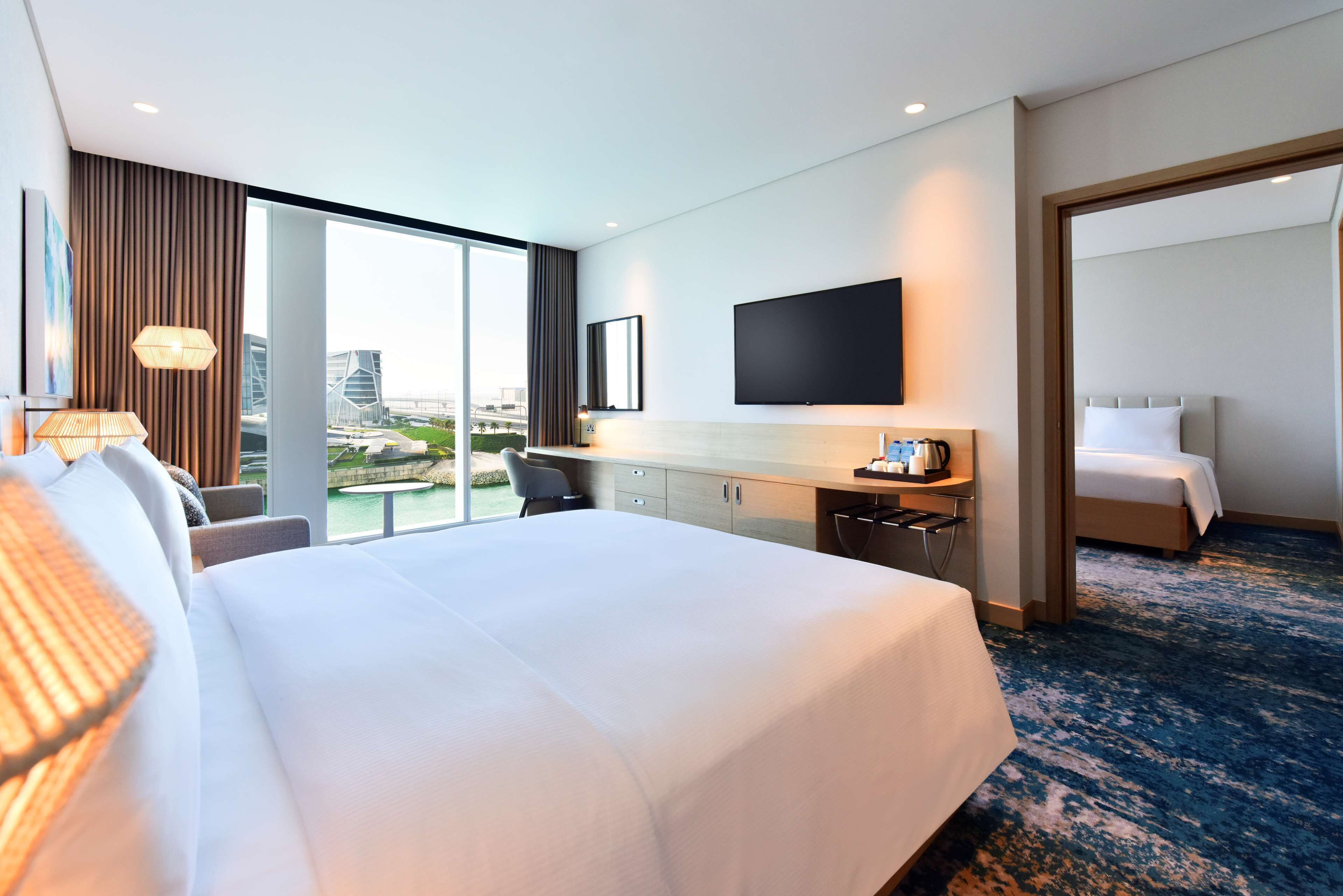 Een hotelkamer met een groot bed, een bureau, een stoel, een flatscreen televisie en uitzicht op een stadsbeeld.