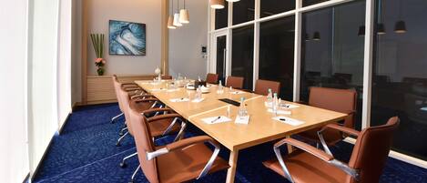 A conference room with a long table, brown chairs, and a blue carpet.