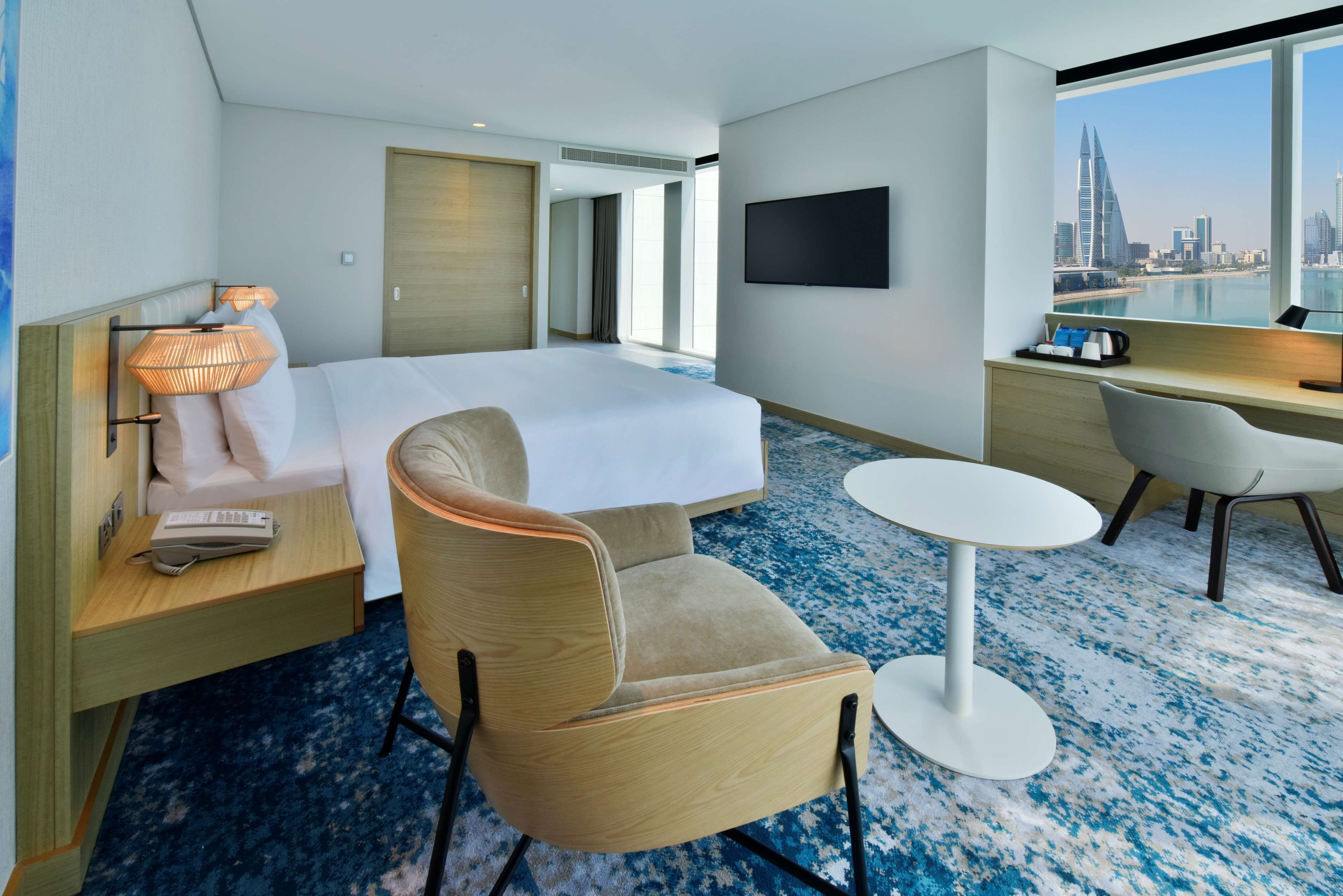 A hotel room with a bed, a desk, a chair, a TV, and a view of a cityscape.
