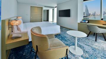A hotel room with a bed, a desk, a chair, a TV, and a view of a cityscape.