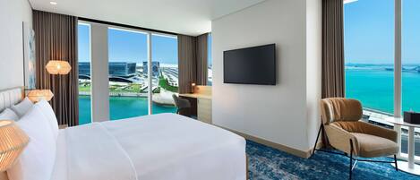 Habitación de hotel con una cama grande, un escritorio, una silla, un televisor y vistas al océano y un puente.