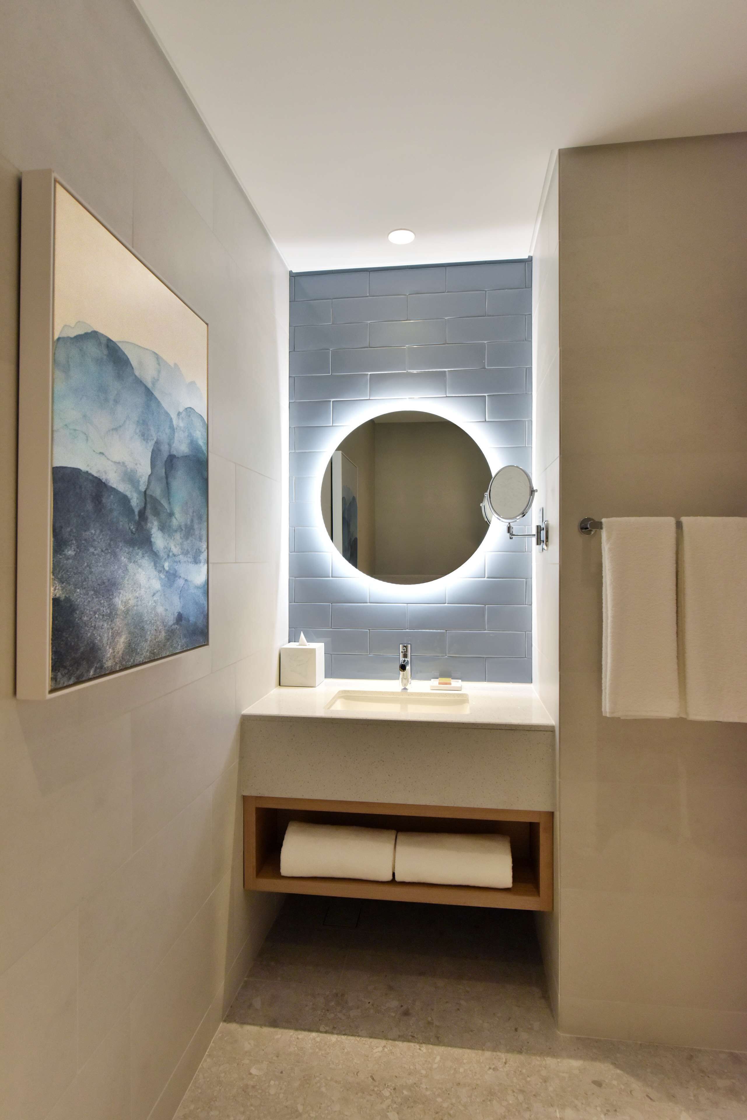 A modern bathroom with a round mirror, a sink, and a towel rack.