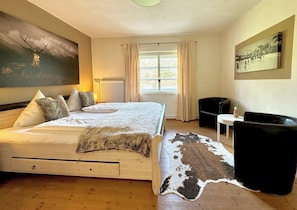 Une chambre à coucher avec un lit en bois, un tapis en peau de vache, un tableau représentant un cerf et une fenêtre avec des rideaux.