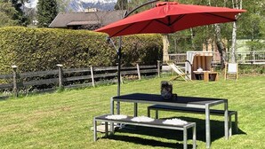 Um pátio com um guarda-sol vermelho, uma mesa e cadeiras, com vista para uma montanha e uma cerca de madeira.