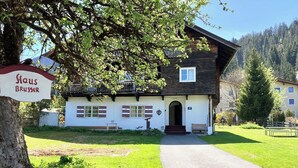 Uma casa de dois andares com fachada branca e telhado escuro, uma entrada frontal com degraus e uma placa com o texto 'Haus Brusser'.