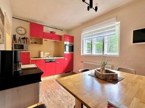 Eine kleine Küche mit roten Schränken, einem Holztisch, einer Uhr und einem Fenster mit Blick.