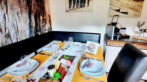 Uma mesa de jantar posta com pratos, copos e talheres, uma jarra e um tabuleiro com comida.
