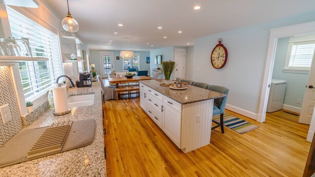 A modern kitchen with a central island, wooden flooring, and built-in cabinetry. - Blue Haven Home, Fire Pit & Blocks from Beach (Cape Charles)
