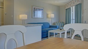 Ein Zimmer mit einem blauen Sofa, einem weißen Tisch und einem weißen Stuhl. An beiden Seiten des Sofas steht jeweils eine Lampe.