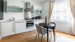 Una cucina moderna con mobili bianchi, piano cottura a gas, forno e zona pranzo con tavolo e sedie.