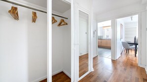 Un appartement moderne avec un plancher en bois, des murs blancs et un coin cuisine visible à travers une porte ouverte.