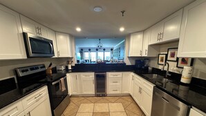 A modern kitchen with white cabinets, a black countertop, stainless steel appliances, and a tiled floor. - "Breakers East 902" Gulf Front 2 BR/2BA Beach setup included (Destin)