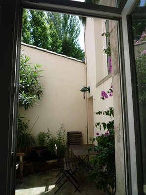 En lille terrasse med et bord og stole, omgivet af krukker med planter og en væg med slyngplanter.