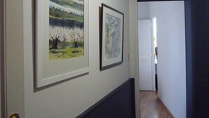 Un couloir avec deux tableaux encadrés accrochés au mur, un banc de couleur sombre et une porte donnant sur une autre pièce.