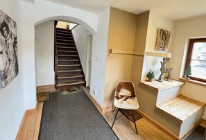 Un escalier menant à l’étage supérieur, une chaise, une petite étagère avec des objets décoratifs et une porte.
