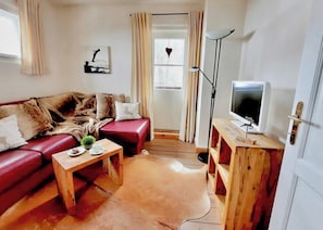 A living room with a red leather sofa, a wooden coffee table, a television on a wooden stand, and a large window with curtains. - Kitz Apartment 3 mit Garten, Nähe Schwarzsee (Kitzbühel)