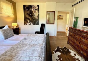 A bedroom with a bed, a large abstract painting, a mirror, a dresser, and a cowhide rug.
